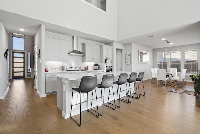 kitchen with wall chimney range hood, a breakfast bar area, appliances with stainless steel finishes, and light wood-style floors