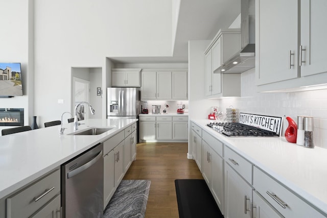 kitchen with tasteful backsplash, stainless steel appliances, light countertops, wall chimney range hood, and a sink