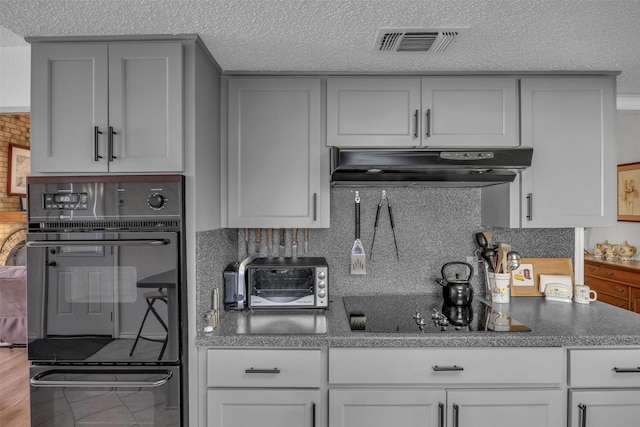 kitchen featuring a toaster, tasteful backsplash, visible vents, under cabinet range hood, and black appliances