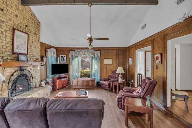 living room featuring beam ceiling, a fireplace, a ceiling fan, wood walls, and wood finished floors