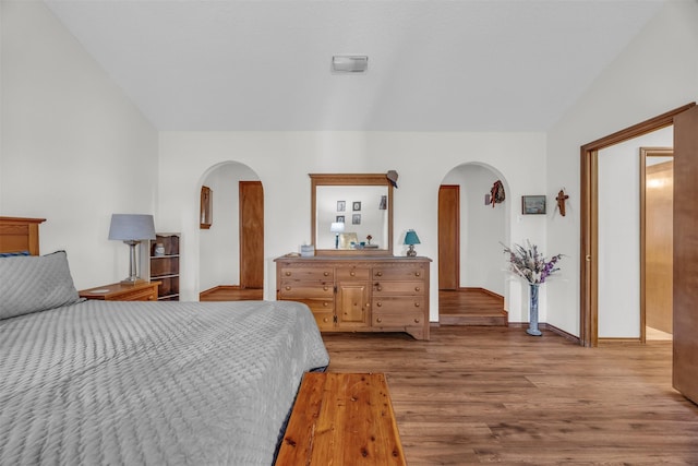 bedroom with arched walkways, vaulted ceiling, and wood finished floors