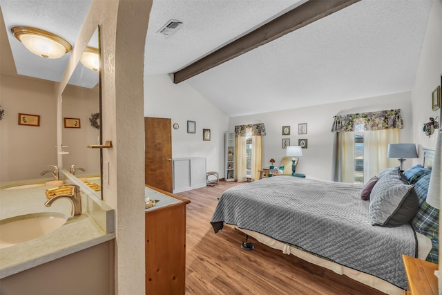 bedroom with visible vents, a sink, lofted ceiling with beams, and wood finished floors