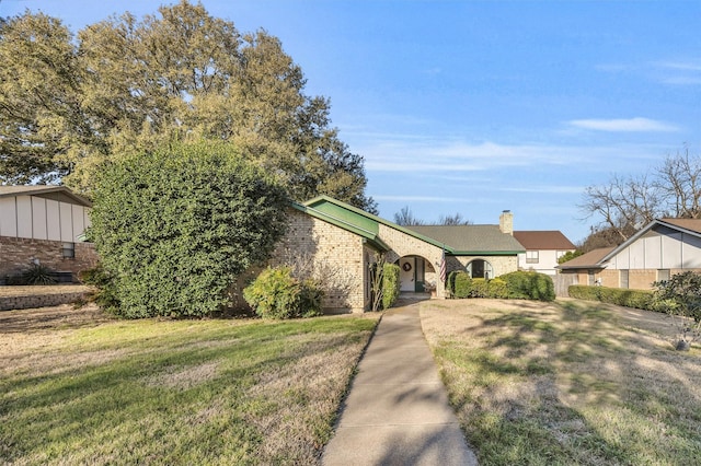 view of front of home with brick siding, a chimney, and a front lawn