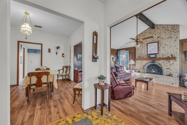 living room with vaulted ceiling with beams, a brick fireplace, visible vents, and wood finished floors