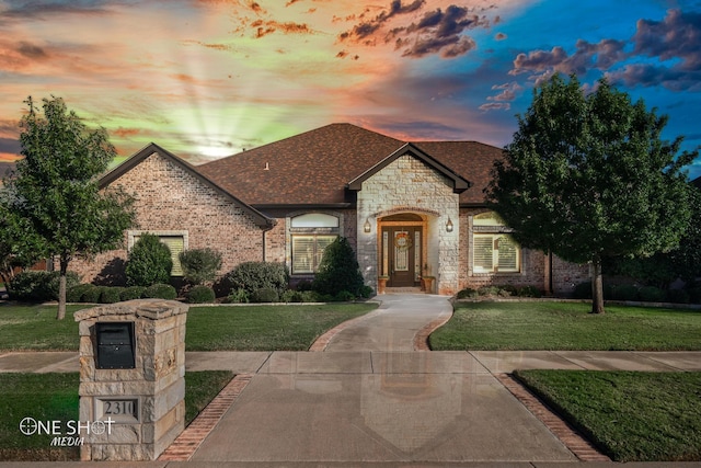 french country home featuring brick siding, a lawn, and roof with shingles