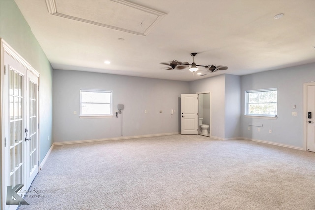 spare room featuring attic access, light colored carpet, baseboards, and ceiling fan