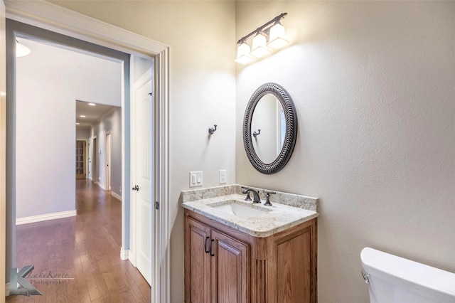 bathroom featuring baseboards, toilet, hardwood / wood-style floors, and vanity