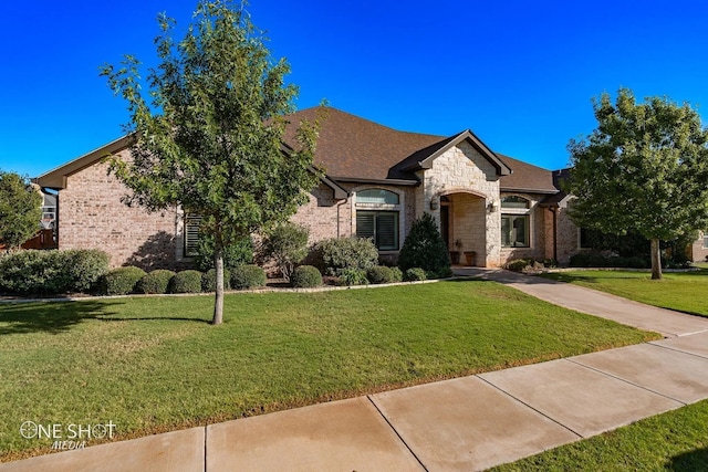 french country home featuring brick siding, stone siding, a shingled roof, and a front lawn