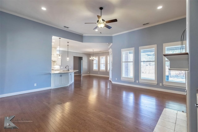 unfurnished living room featuring visible vents, ornamental molding, ceiling fan with notable chandelier, a sink, and dark wood-style flooring