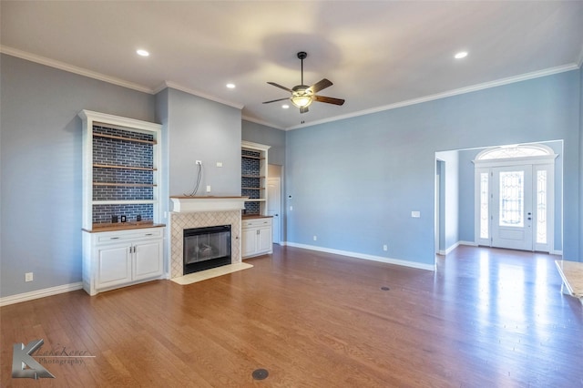 unfurnished living room with a ceiling fan, wood finished floors, baseboards, ornamental molding, and a tile fireplace