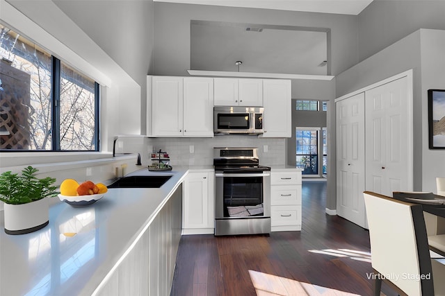 kitchen with dark wood-style flooring, stainless steel appliances, light countertops, decorative backsplash, and white cabinetry