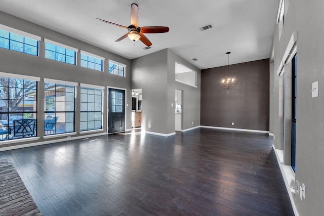 unfurnished living room featuring dark wood-style floors, visible vents, a towering ceiling, baseboards, and ceiling fan with notable chandelier