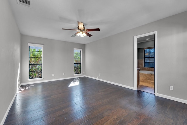 spare room with dark wood-style flooring, visible vents, ceiling fan, and baseboards