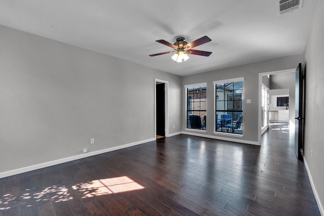 empty room with dark wood-style floors, a ceiling fan, visible vents, and baseboards