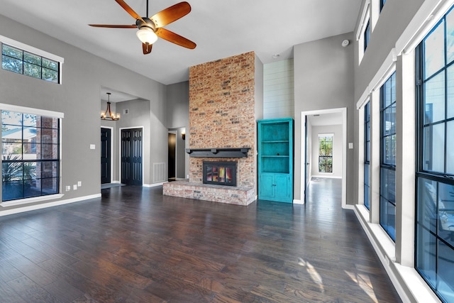 unfurnished living room with a fireplace, a towering ceiling, wood finished floors, baseboards, and ceiling fan with notable chandelier