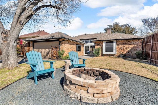 back of house featuring an outdoor fire pit, a garage, brick siding, fence, and a chimney