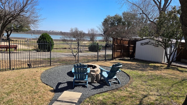 view of yard with an outbuilding, a storage unit, a water view, fence, and a fire pit