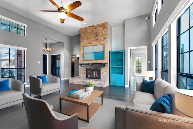 living area featuring ceiling fan with notable chandelier, a fireplace, a towering ceiling, and wood finished floors