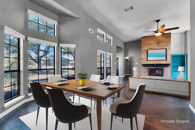 dining space with a large fireplace, a high ceiling, visible vents, a ceiling fan, and dark wood-style floors