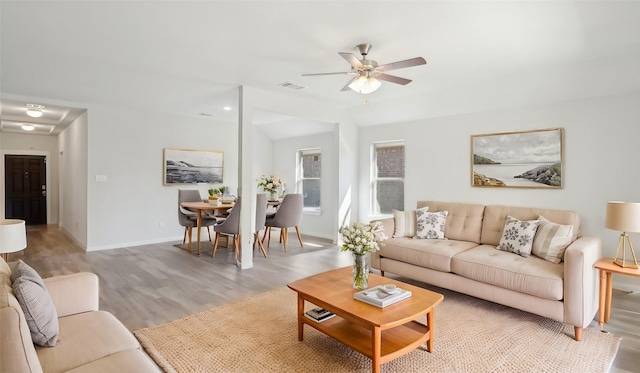 living area with lofted ceiling, visible vents, light wood-style floors, a ceiling fan, and baseboards