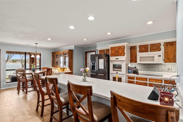 kitchen with tasteful backsplash, light countertops, brown cabinetry, ornamental molding, and black appliances