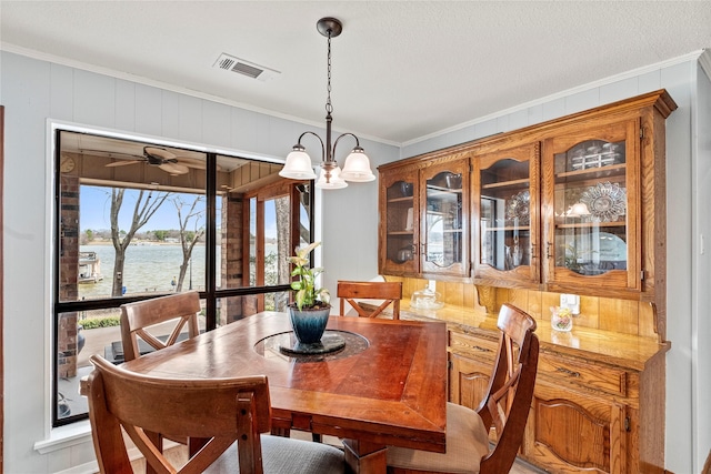 dining space featuring ornamental molding, visible vents, a water view, and a ceiling fan