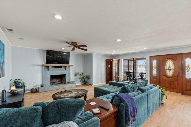 living area with a brick fireplace, a textured ceiling, baseboards, and wood finished floors