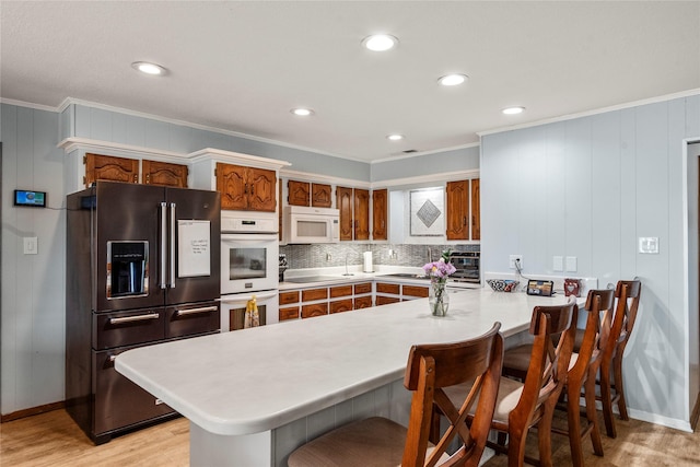 kitchen featuring light wood-style flooring, a peninsula, light countertops, black appliances, and tasteful backsplash