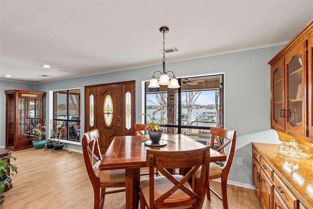 dining area featuring visible vents, a textured ceiling, light wood finished floors, and an inviting chandelier