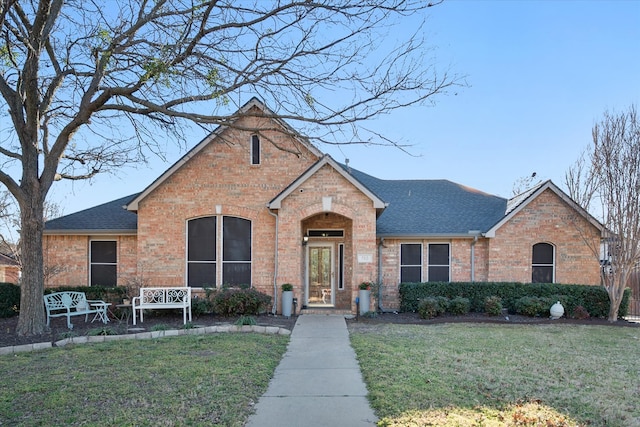 view of front of home featuring a front yard, brick siding, and roof with shingles