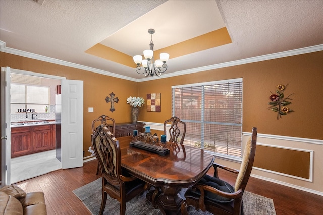 dining area with wood finished floors, an inviting chandelier, a tray ceiling, crown molding, and a textured ceiling