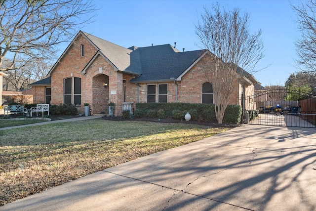 view of front of property featuring a shingled roof, a gate, a front lawn, and brick siding