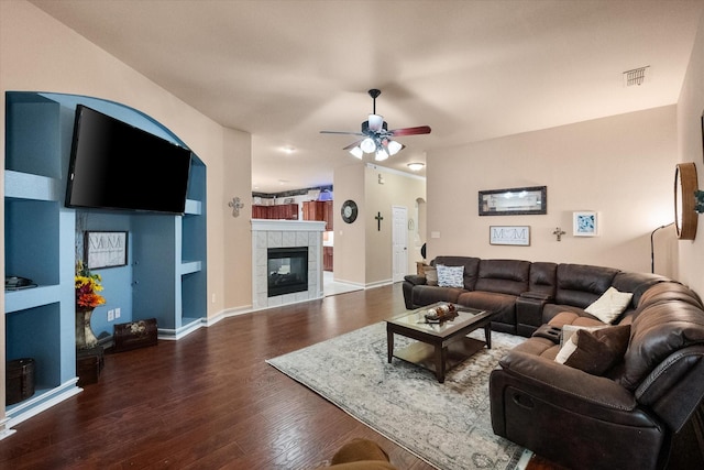 living area with visible vents, a tiled fireplace, ceiling fan, wood finished floors, and baseboards