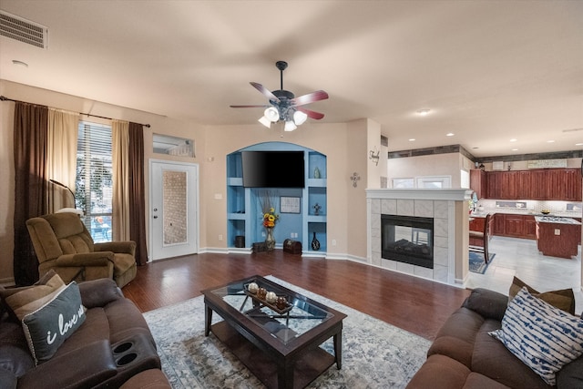 living room featuring visible vents, a tiled fireplace, ceiling fan, wood finished floors, and baseboards