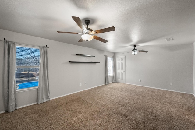 spare room with a textured ceiling, ceiling fan, carpet floors, visible vents, and baseboards