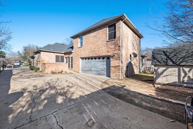 exterior space featuring a garage, brick siding, an outdoor structure, fence, and driveway