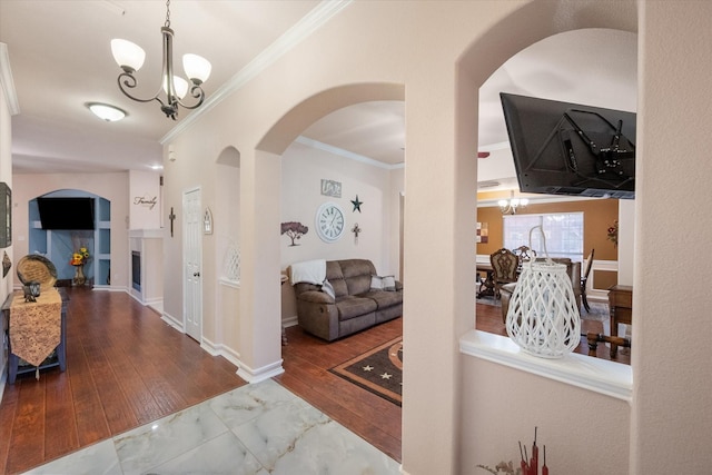 hallway featuring arched walkways, baseboards, wood-type flooring, ornamental molding, and a chandelier