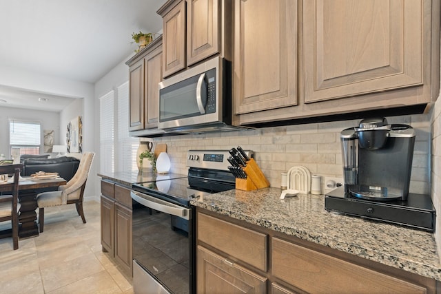 kitchen with backsplash, appliances with stainless steel finishes, light tile patterned flooring, light stone countertops, and baseboards