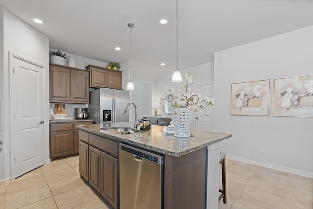 kitchen featuring an island with sink, appliances with stainless steel finishes, light stone countertops, pendant lighting, and a sink