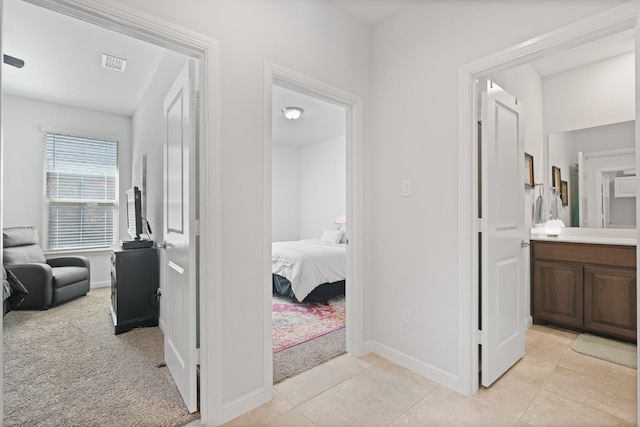 hallway with light carpet, light tile patterned floors, visible vents, and baseboards