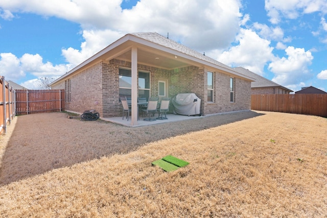 rear view of house featuring brick siding, a fenced backyard, a yard, and a patio