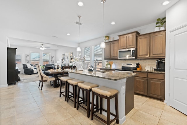 kitchen featuring a breakfast bar, backsplash, appliances with stainless steel finishes, a sink, and dark stone countertops