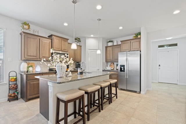 kitchen with a breakfast bar, stainless steel refrigerator with ice dispenser, decorative backsplash, stone countertops, and a sink