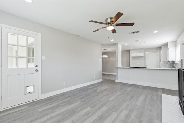 unfurnished living room featuring ceiling fan with notable chandelier, recessed lighting, light wood-type flooring, and baseboards