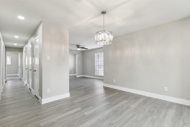 spare room featuring recessed lighting, baseboards, light wood finished floors, and ceiling fan with notable chandelier