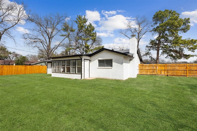 back of property with brick siding, a lawn, a chimney, and a fenced backyard