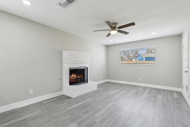 unfurnished living room with baseboards, visible vents, ceiling fan, wood finished floors, and a fireplace