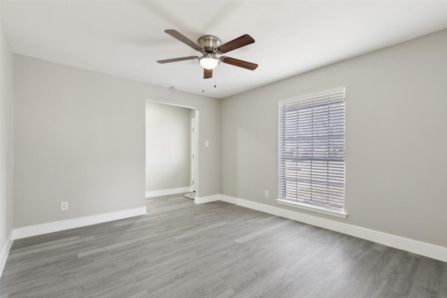 spare room with wood finished floors, a ceiling fan, and baseboards