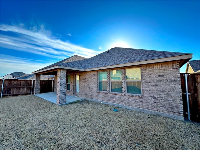 back of property with a patio area, a shingled roof, fence, and brick siding