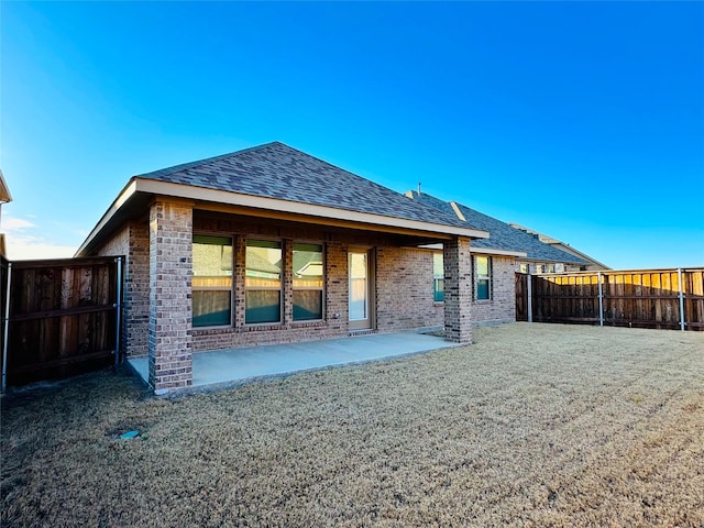 back of property featuring a shingled roof, a lawn, a fenced backyard, a patio area, and brick siding